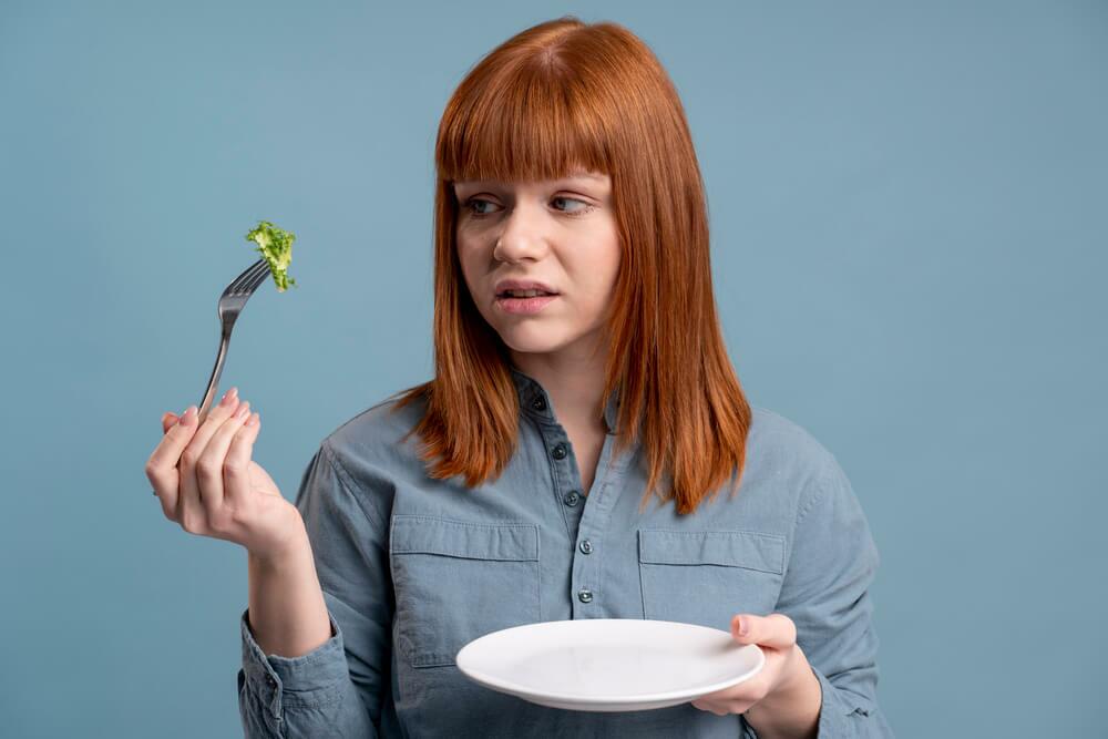 Garota com desnutrição ou distúrbios alimentares tentando comer um brócolis